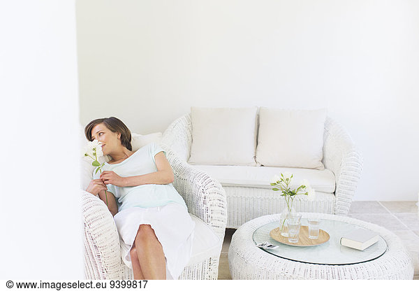 Woman smelling flowers in wicker chair in living room