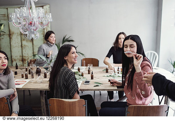 Woman smelling litmus strip while sitting amidst multi-ethnic colleagues at perfume workshop