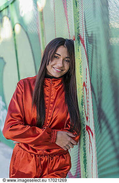 Woman smiling while leaning on graffiti fence