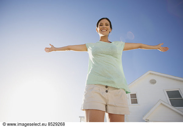 Woman smiling with arms outstretched against blue sky