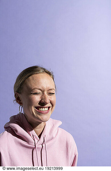 Woman smiling with eyes closed against purple background in studio