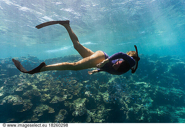 Woman snorkeling with sun rays and coral reef