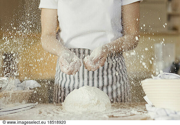 Woman sprinkling flour on dough at home