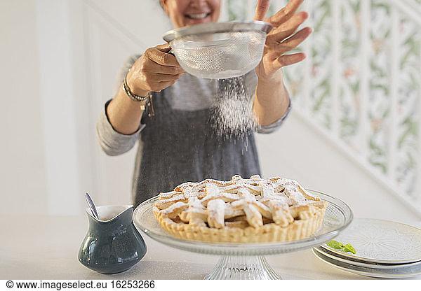 Woman sprinkling fresh baked apple pie with powdered sugar