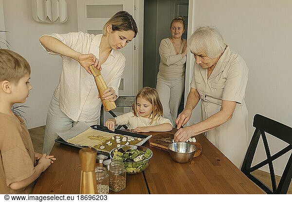 Woman sprinkling pepper on food by family at home