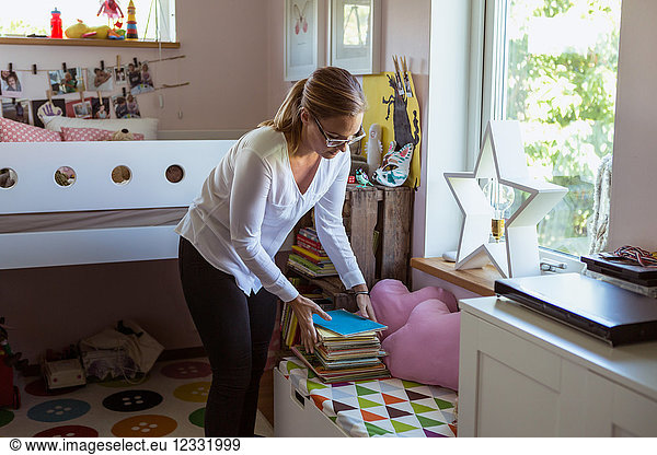 Woman stacking books on table while cleaning bedroom at home