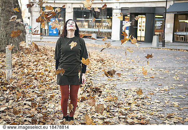 Woman standing amidst falling autumn leaves on footpath