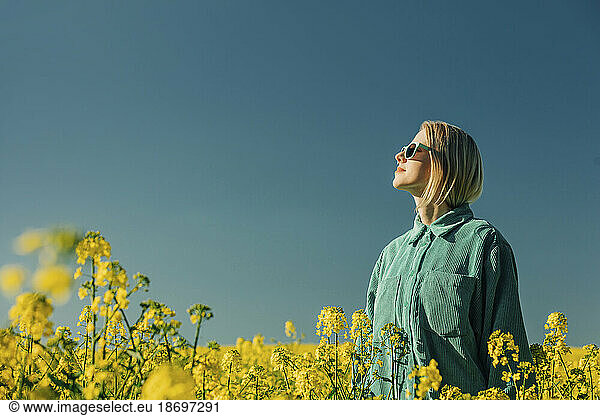 Woman standing amidst flowers in rapeseed field at sunny day