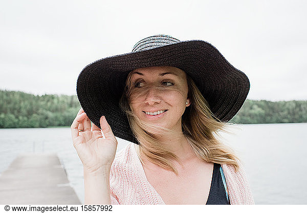 woman standing at a windy beach smiling with a hat on