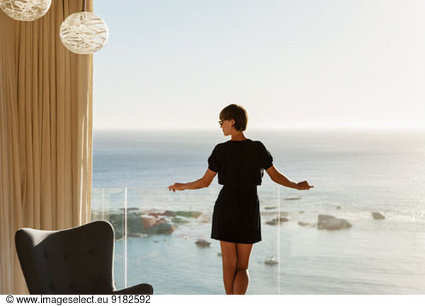 Woman standing at balcony railing overlooking ocean