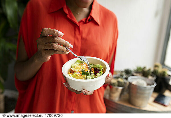 Woman standing at home eating bowl of salad