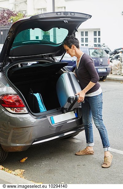Woman standing beside car  putting suitcase in open boot
