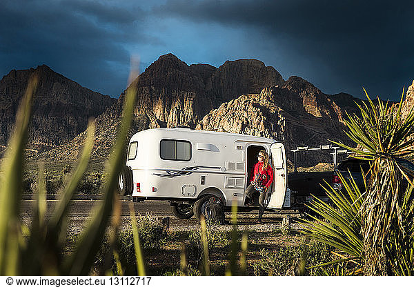 Woman standing by camper trailer against mountains and sky