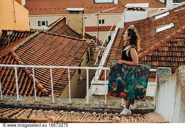 Woman standing holding abstract art painting while standing on roof