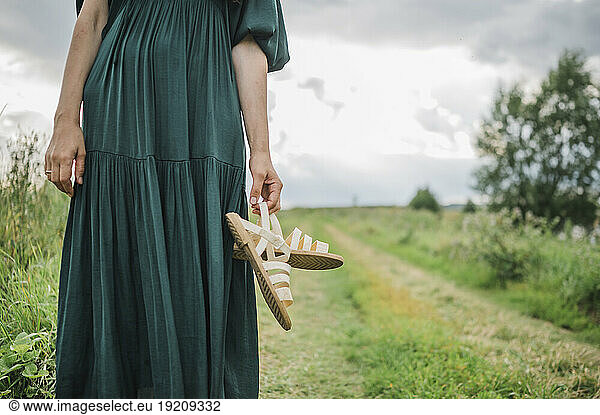 Woman standing holding footwear in field