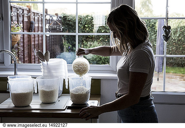 Woman standing in a domestic kitchen  making jar candles.