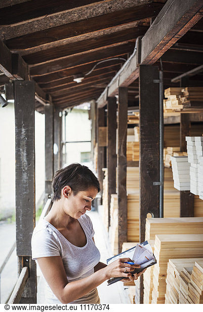 Woman standing in a lumber yard  holding a folder  checking notes.