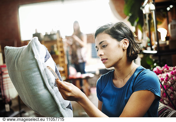 Woman standing in a shop holding a cushion  reading the price tag.