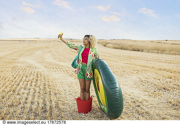 Woman standing in bucket with avocado shaped inflatable ring looking at hand mirror