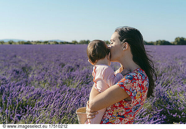 Woman standing in vast lavender field with baby girl in hands