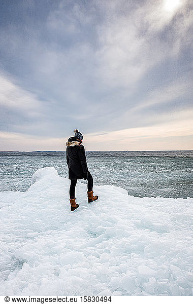 Woman standing on icy shoreline of a lake looking into the distance.