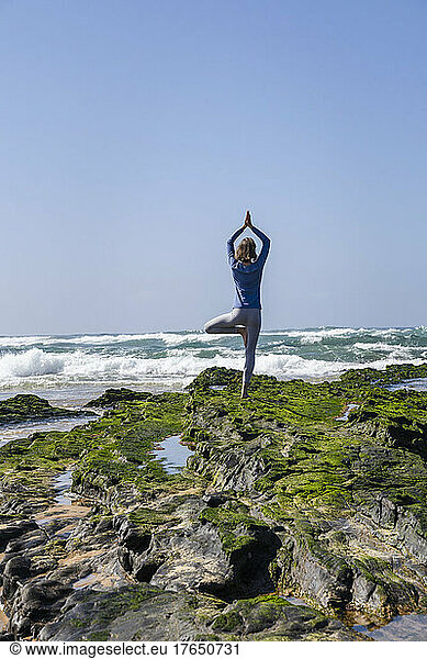 Woman standing on rock practicing tree pose doing yoga at beach
