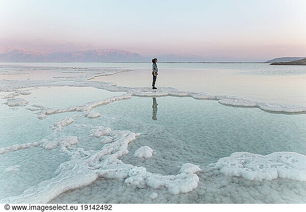 Woman standing on salt formations in dead sea at sunset