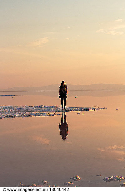 Woman standing on shore by Great Salt Lake during sunset
