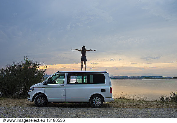 Woman standing on top of the van resting at sunset on the lake
