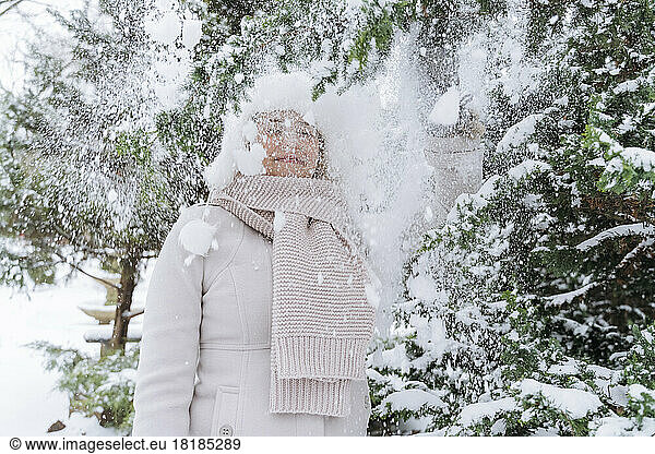Woman standing under falling powdered snow by tree