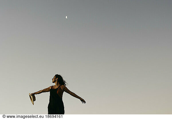 Woman standing with arms outstretched under sky with moon