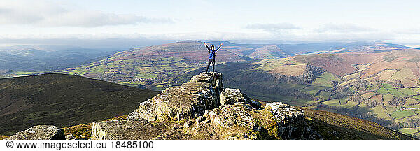 Woman standing with arms raised at top of hill