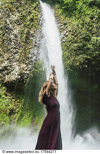 Woman standing with arms raised in front of La Fortuna Waterfall  Costa Rica