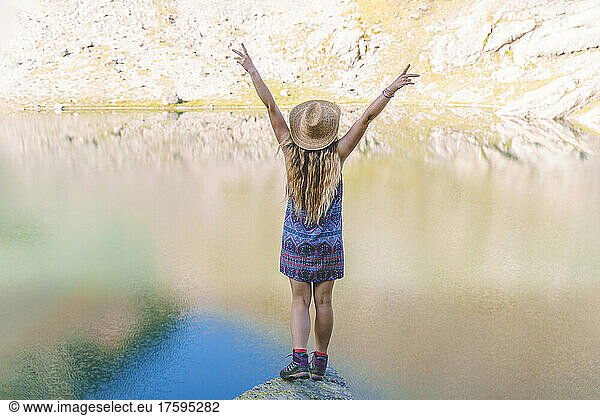 Woman standing with arms raised on rock in lake