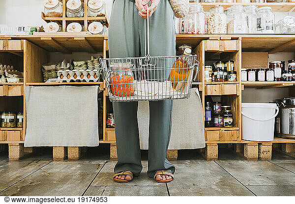 Woman standing with basket of groceries in shop
