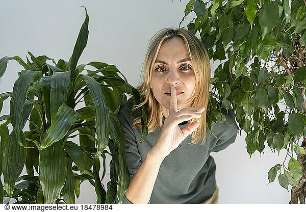 Woman standing with finger on lips amidst plants