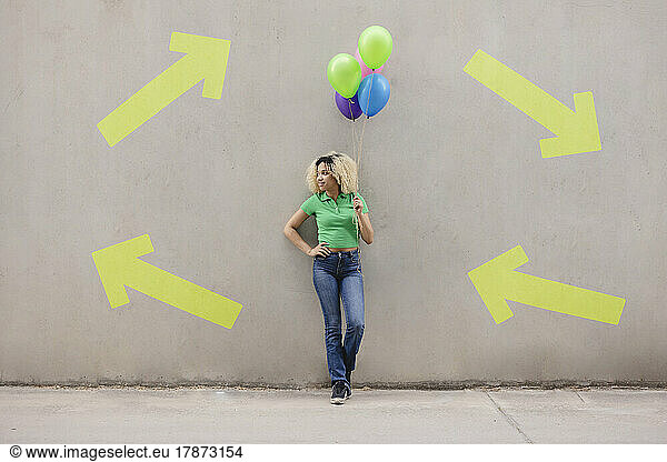 Woman standing with hand on hip standing with multi colored balloons in front of wall