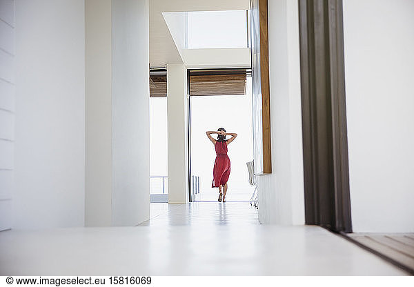 Woman standing with hands behind head in home corridor