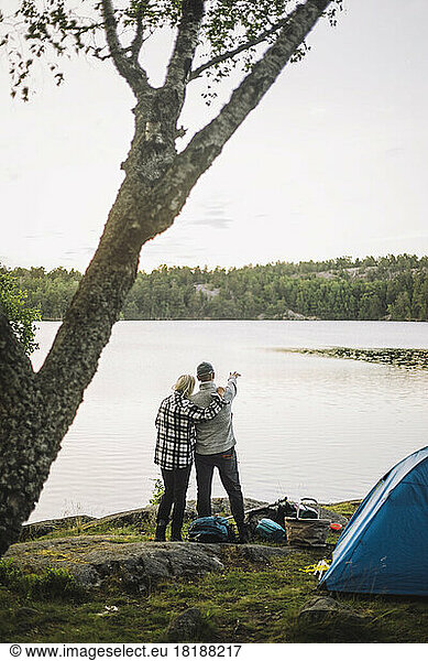 Woman standing with man looking at view from lakeshore
