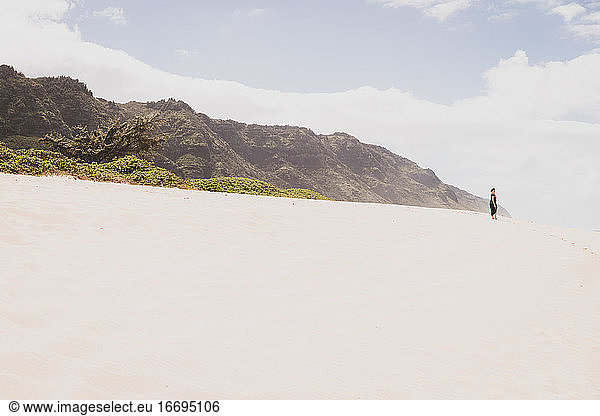 Woman stands on a sandy hill in front of a mountain in the distance