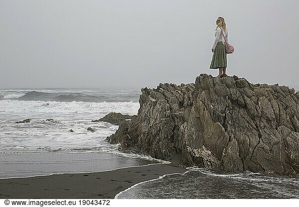 Woman stands on rock above foggy coastline