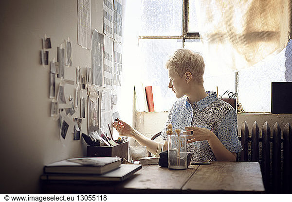 Woman sticking photographs on wall while sitting by table at home