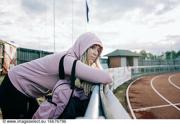woman stood by a running track looking thoughtful