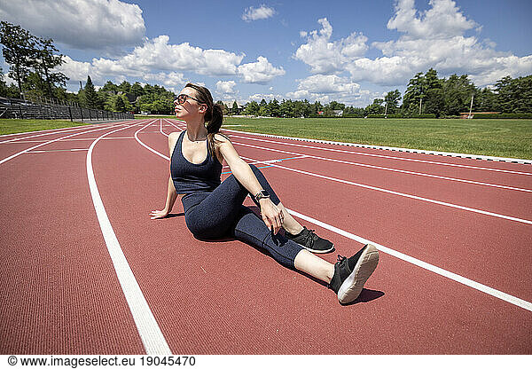 woman stretches in the sun while working out on a track