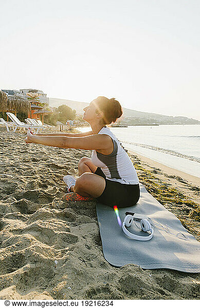 Woman stretching arms sitting on exercise mat at beach