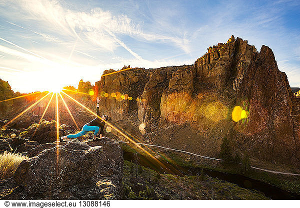 Woman stretching on rock against mountains at Smith Rock State Park on sunny day