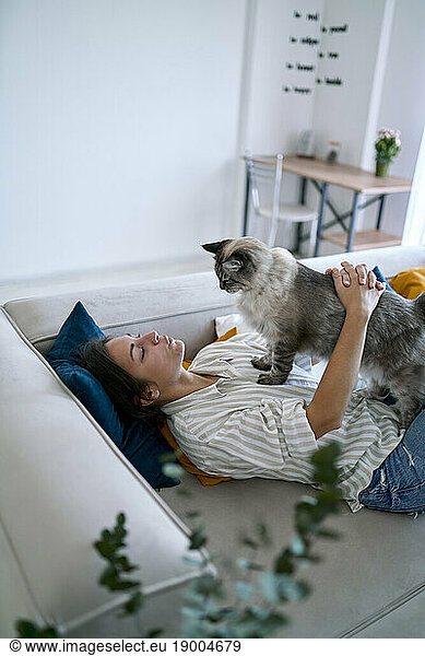 Woman stroking cat on sofa at home