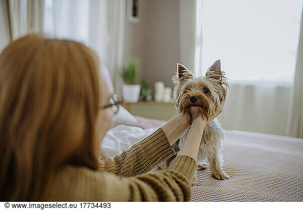 Woman stroking pet dog sitting on bed at home