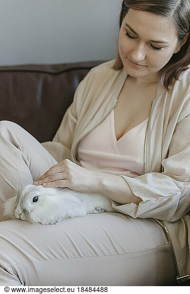 Woman stroking rabbit on lap at home