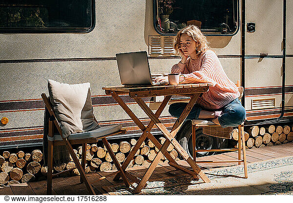 Woman study with laptop near trailer outdoors.
